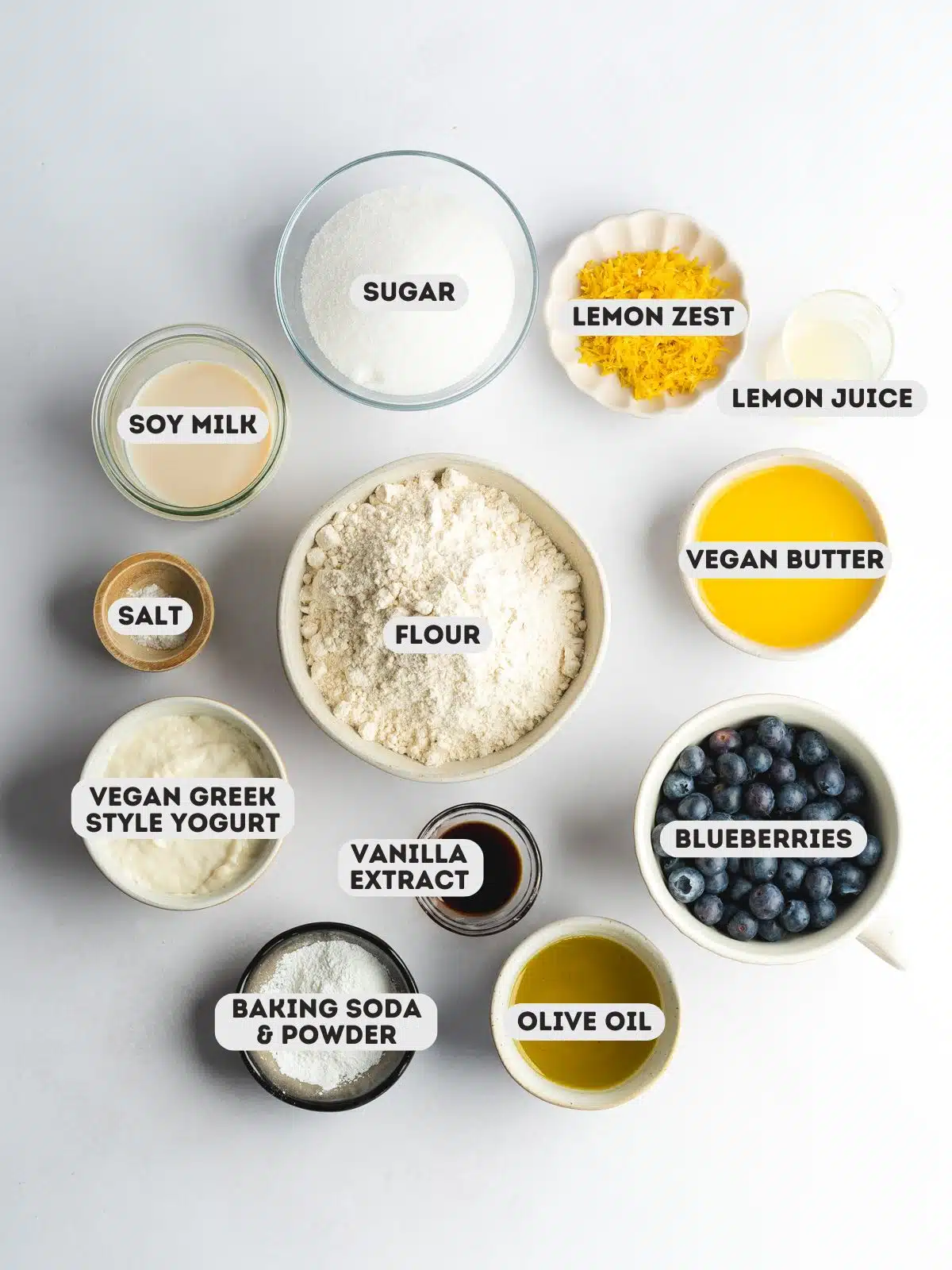 ingredients for vegan blueberry lemon cake measured out in bowls on a light gray surface.