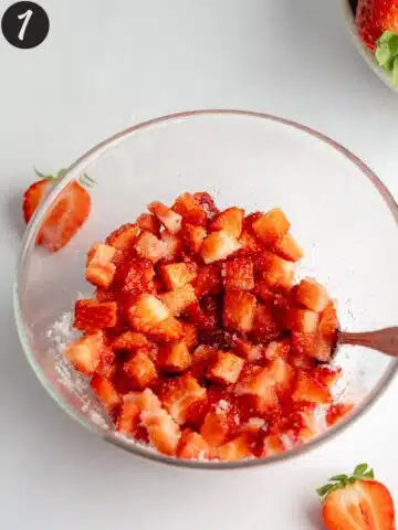 strawberries and sugar macerating in a clear bowl.