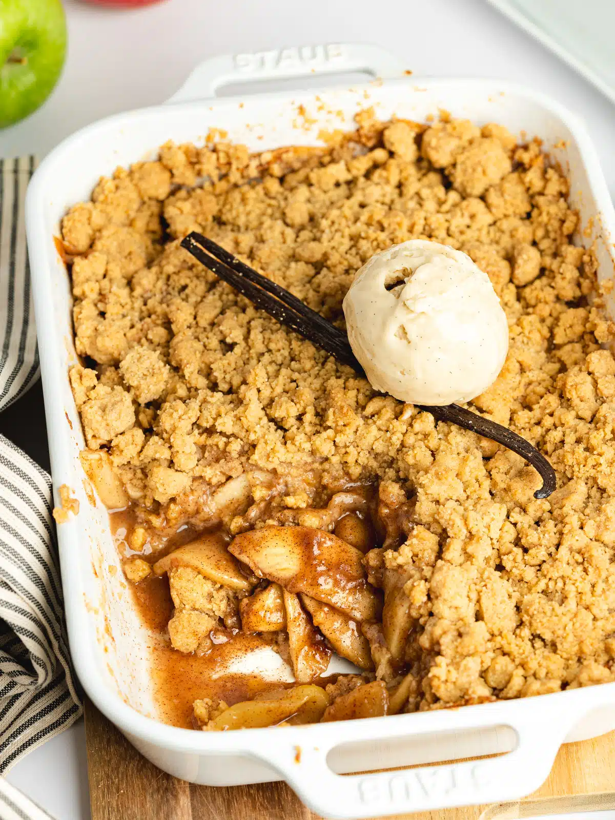vegan apple crumble with a scoop of vanilla ice cream and a vanilla pod on top.