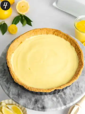 shortcrust pastry tart shell with creamy lemon filling on a marble plate.