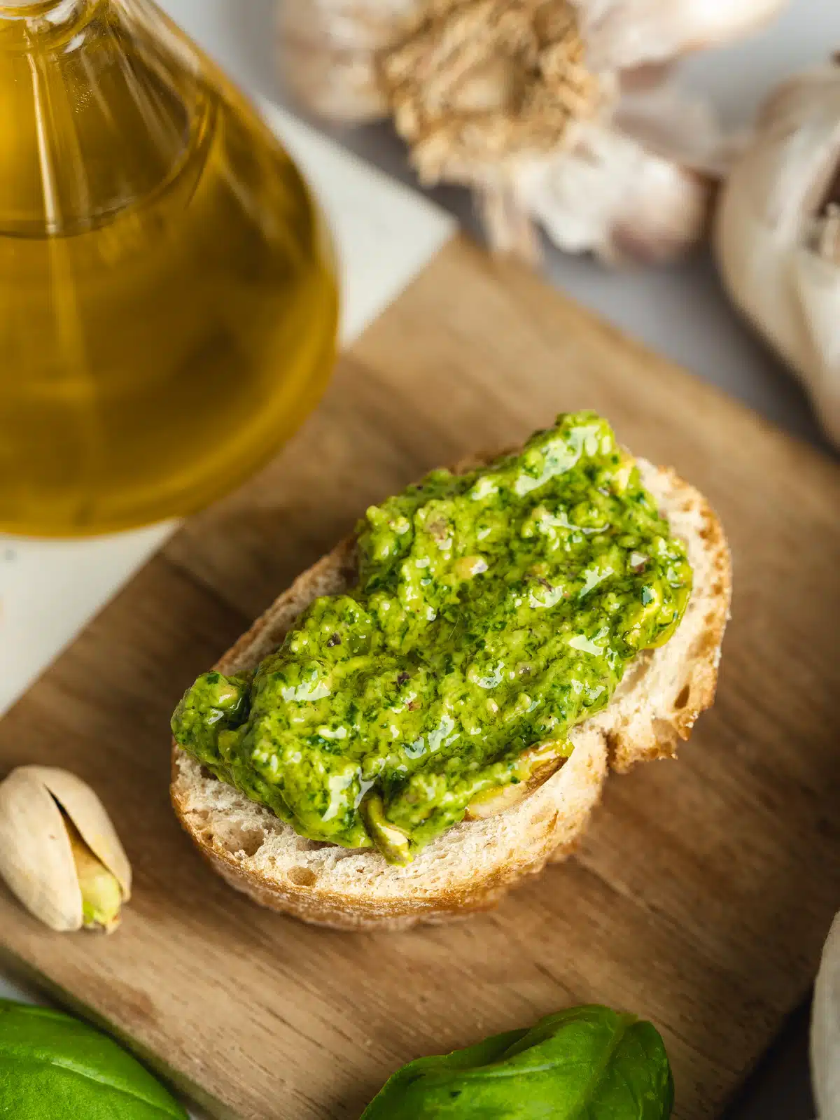 a slice of crusty bread on a wooden cutting board with a thick slathering of pistachio pesto spread on top.