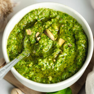 pistachio basil pesto in a white bowl with a spoon showing the bright colour and chunky textures.