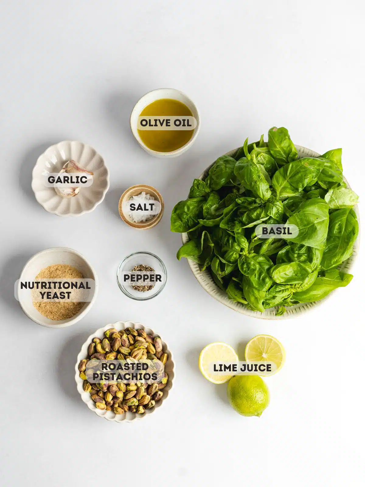ingredients to make fresh basil pesto with pistachios measured out in bowls on a light gray surface.