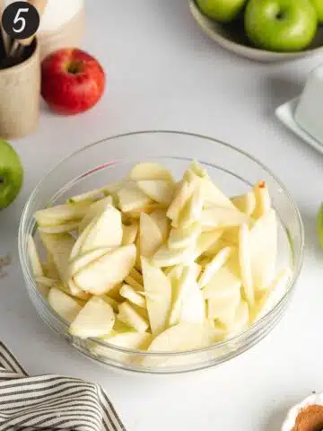 sliced apples in a large mixing bowl with a coating of apple cider vinegar.