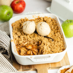 a white staub dish with apple crumble and two scoops of vanilla ice cream on top.