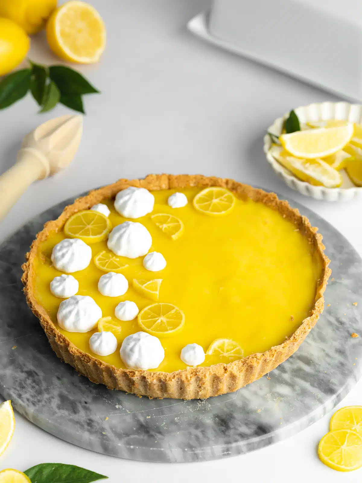 a lemon tart with piped whipped cream and lemon slices on top of a marble plate.