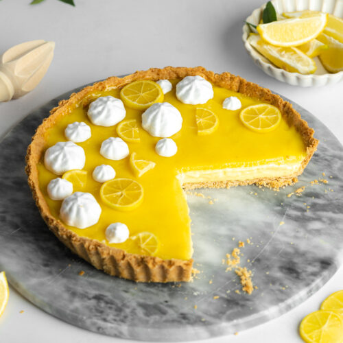 a vegan lemon tart with lemon curd topping and a few slices taken from it showing the creamy filling.