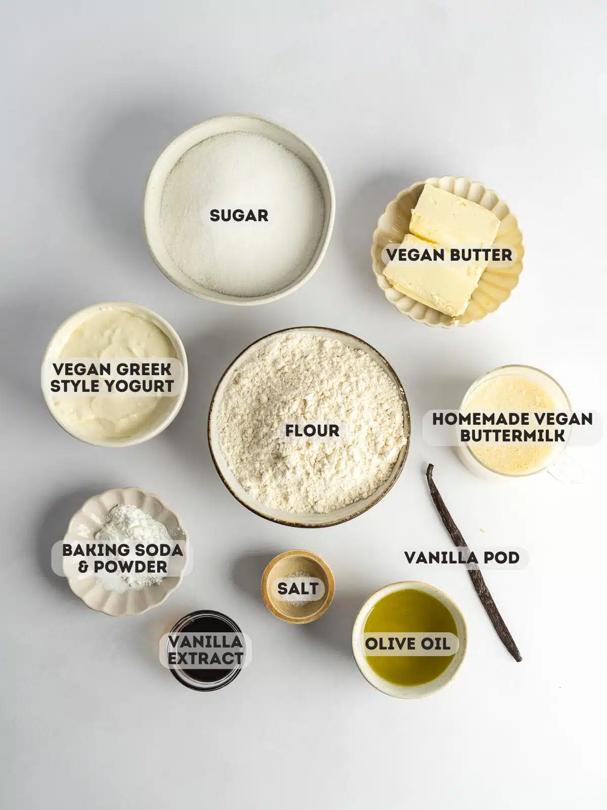 ingredients to make vegan vanilla cake measured out in bowls on a light gray surface with text overlay.