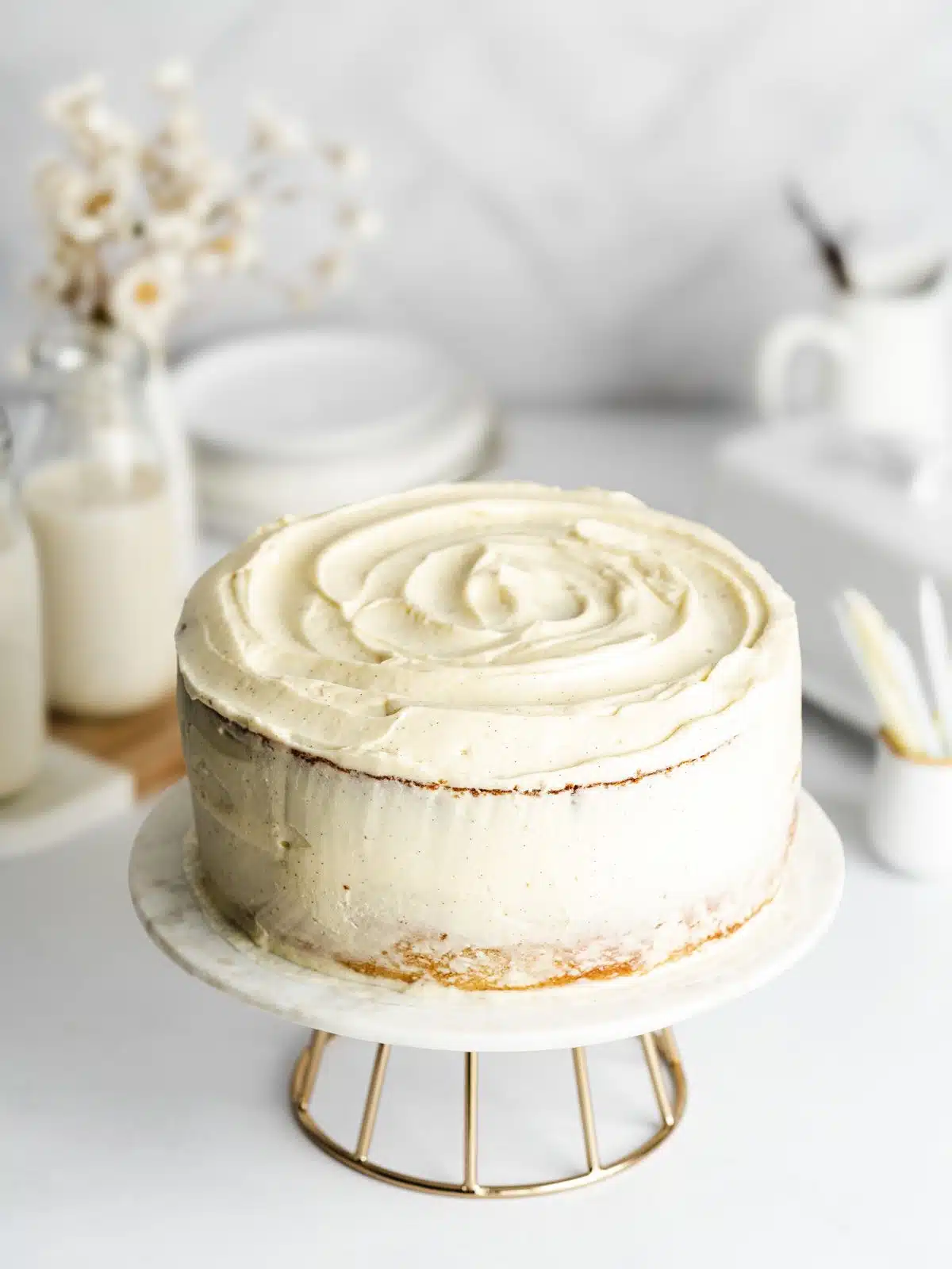 a vanilla cake with swirled vanilla frosting on a marble cake stand with a white background.
