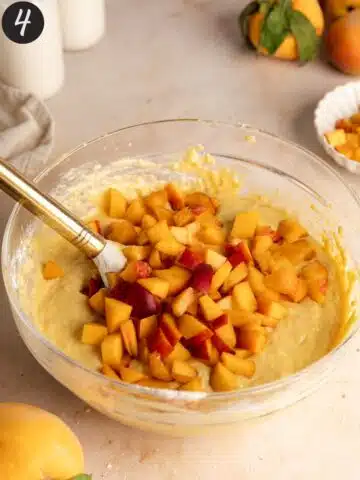 a mixing bowl with peach muffin batter and fresh peach chunks thrown in on top before mixing.