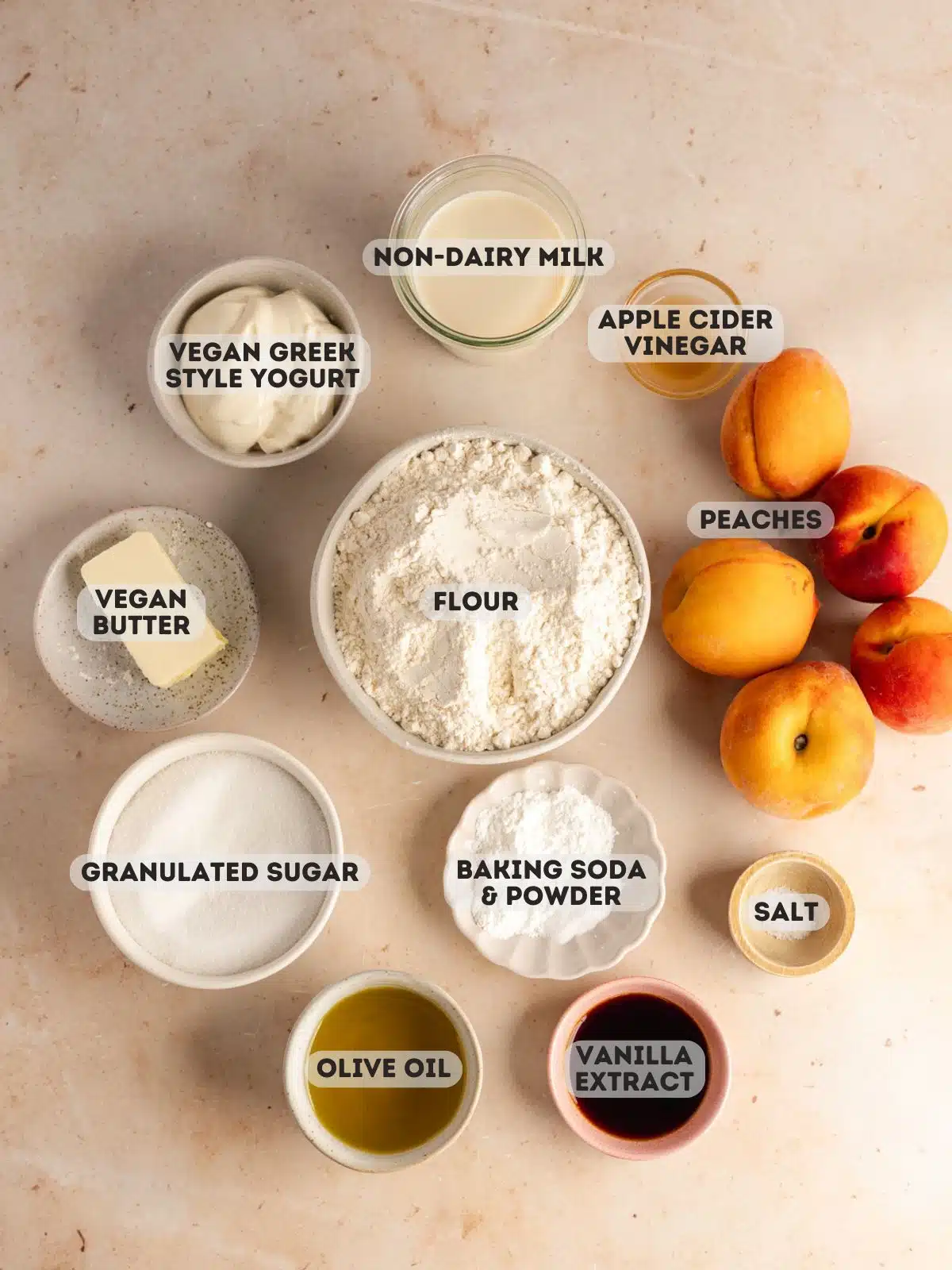ingredients to make peach cobbler muffins measured out in bowls on a peach colored surface.