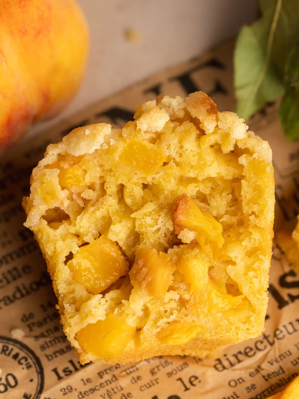 a peach muffin that's been sliced in half showing the fluffy interior studded with fresh peach chunks.