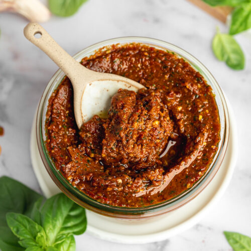 a weck jar with sundried tomato pesto and olive oil drizzled on top with a ceramic spoonful showing the thick consistency-
