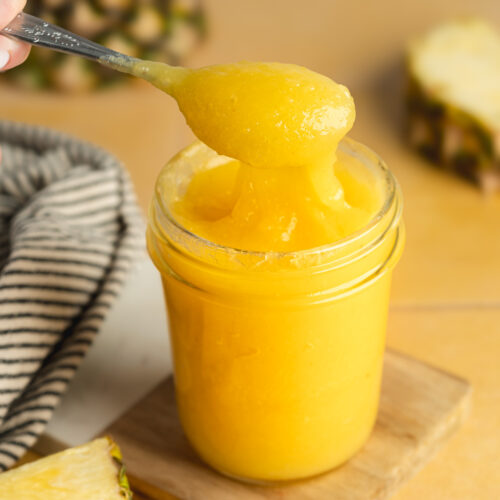 a jar of fresh pineapple curd with a spoon showing the thick and glossy consistency.