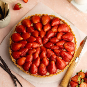 a strawberry tart topped with glazed strawberries on a pink surface.