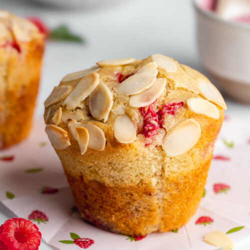 a raspberry almond muffin with toasted almond topping on raspberry parchment paper.