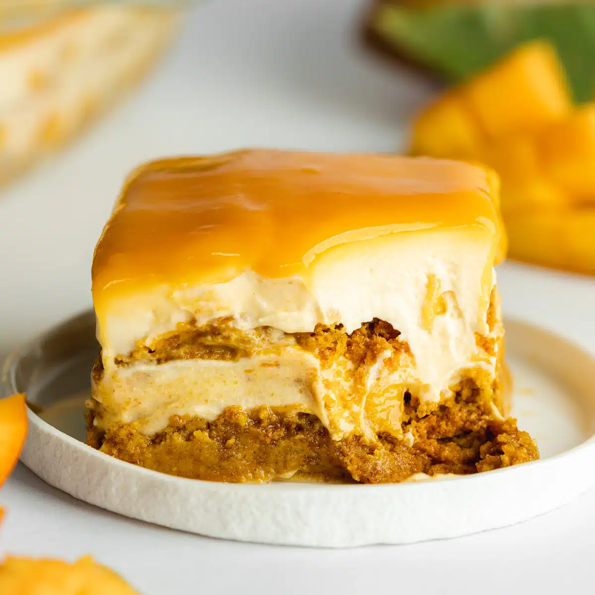 a slice of mango tiramisu on a small white ceramic plate with a spoonful taken from it showing the creamy consistency.