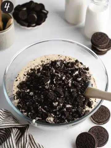 chopped and crushed oreo cookies in a bowl with creamy cheesecake filling before being folded.