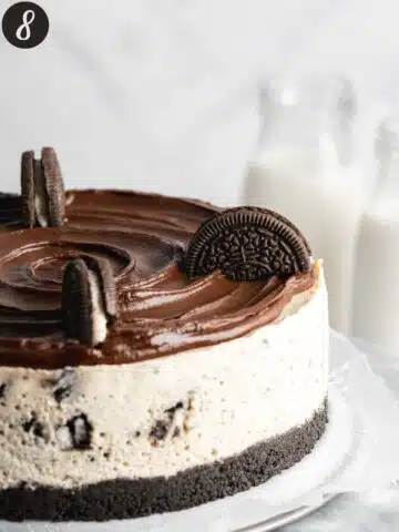 oreo cheesecake with ganache topping and some oreo cookie halves being added around the top.