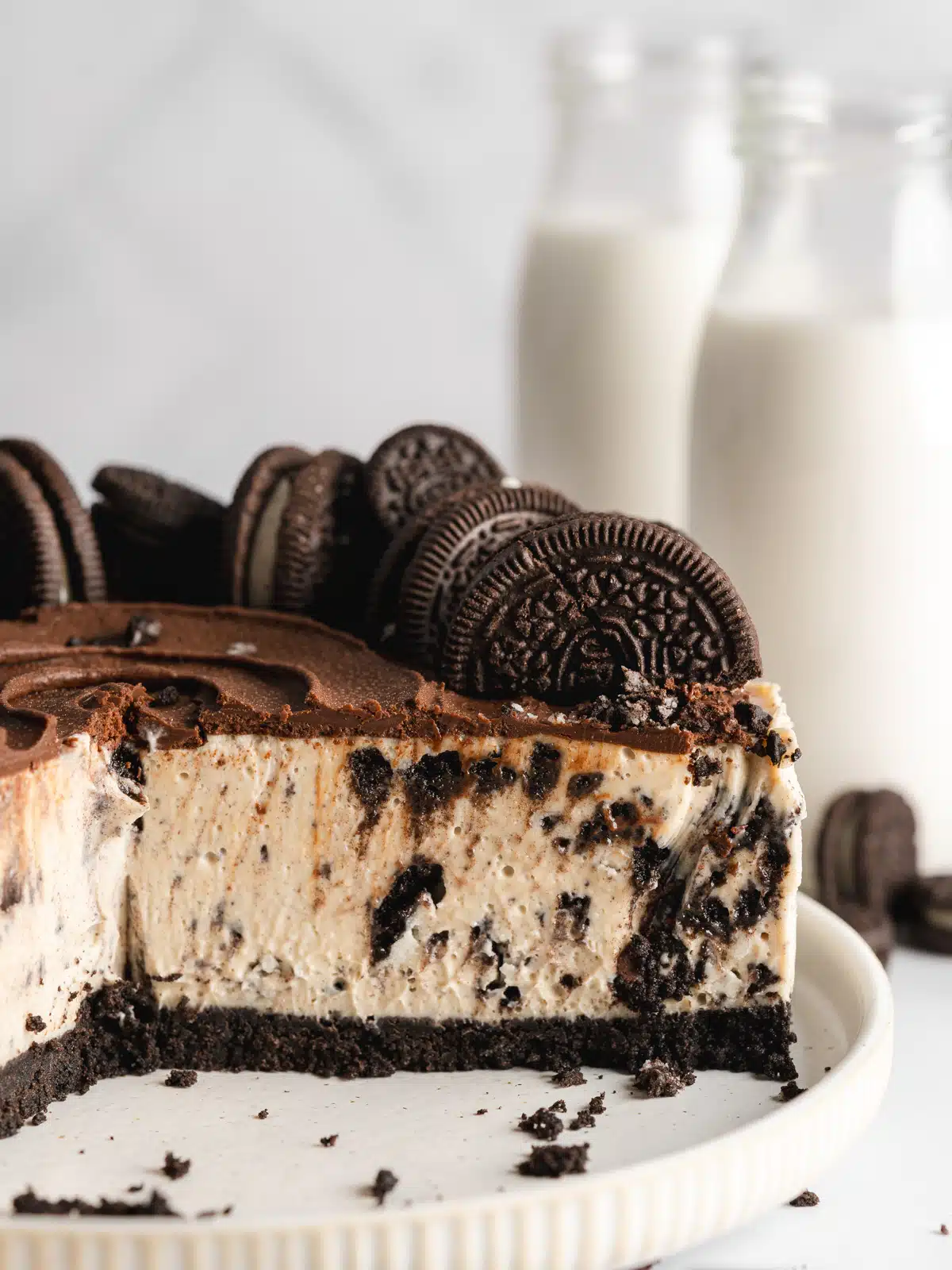 oreo cheesecake with oreo topping and creamy cookie filling and 2 milk bottles in the background.