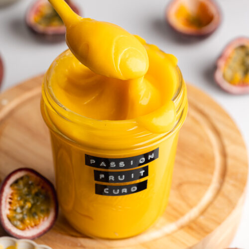 a jar with homemade passion fruit curd and a spoon lifting some out showing the smooth thick consistency.