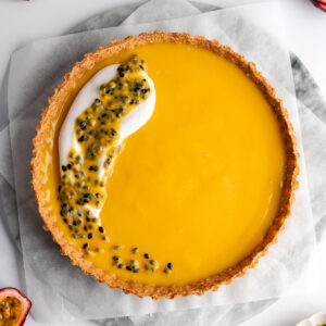 a passion fruit curd filled tart with a dollop of coconut cream and fresh passionfruit on top.