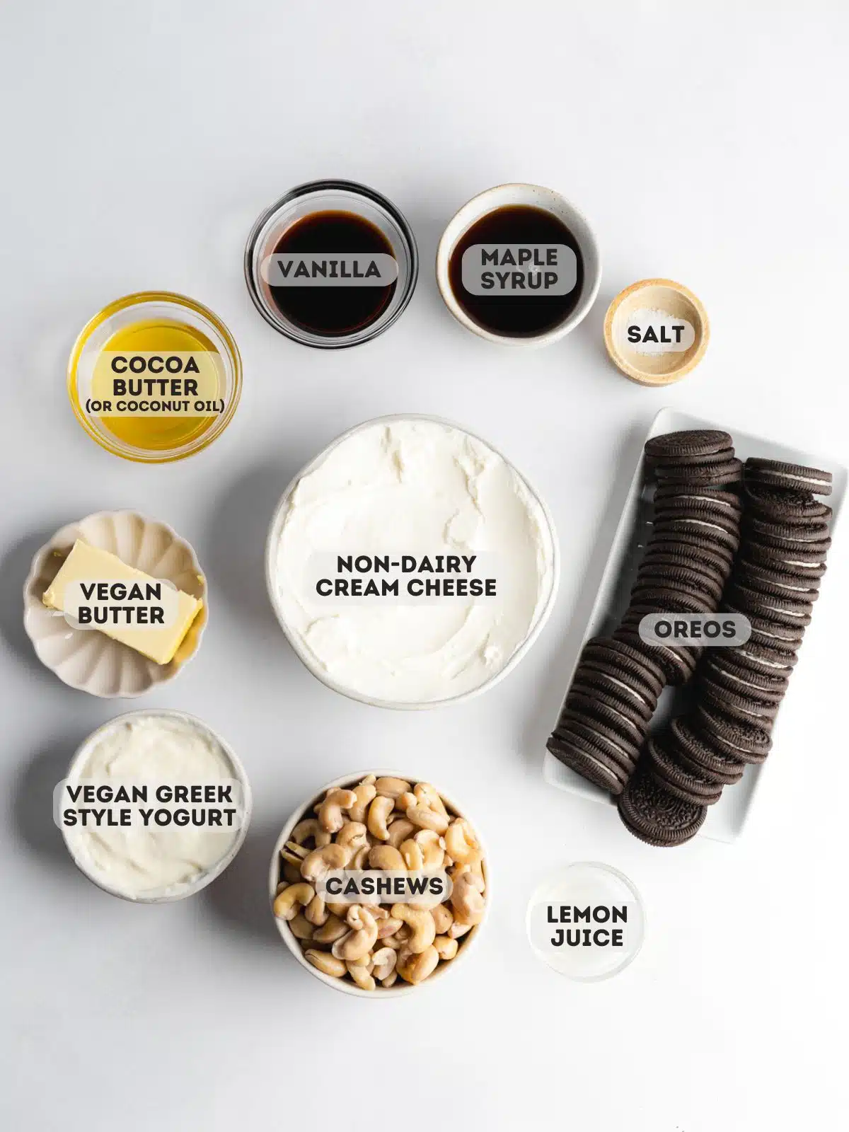ingredients for vegan oreo cheesecake measured out in bowls on a white surface.