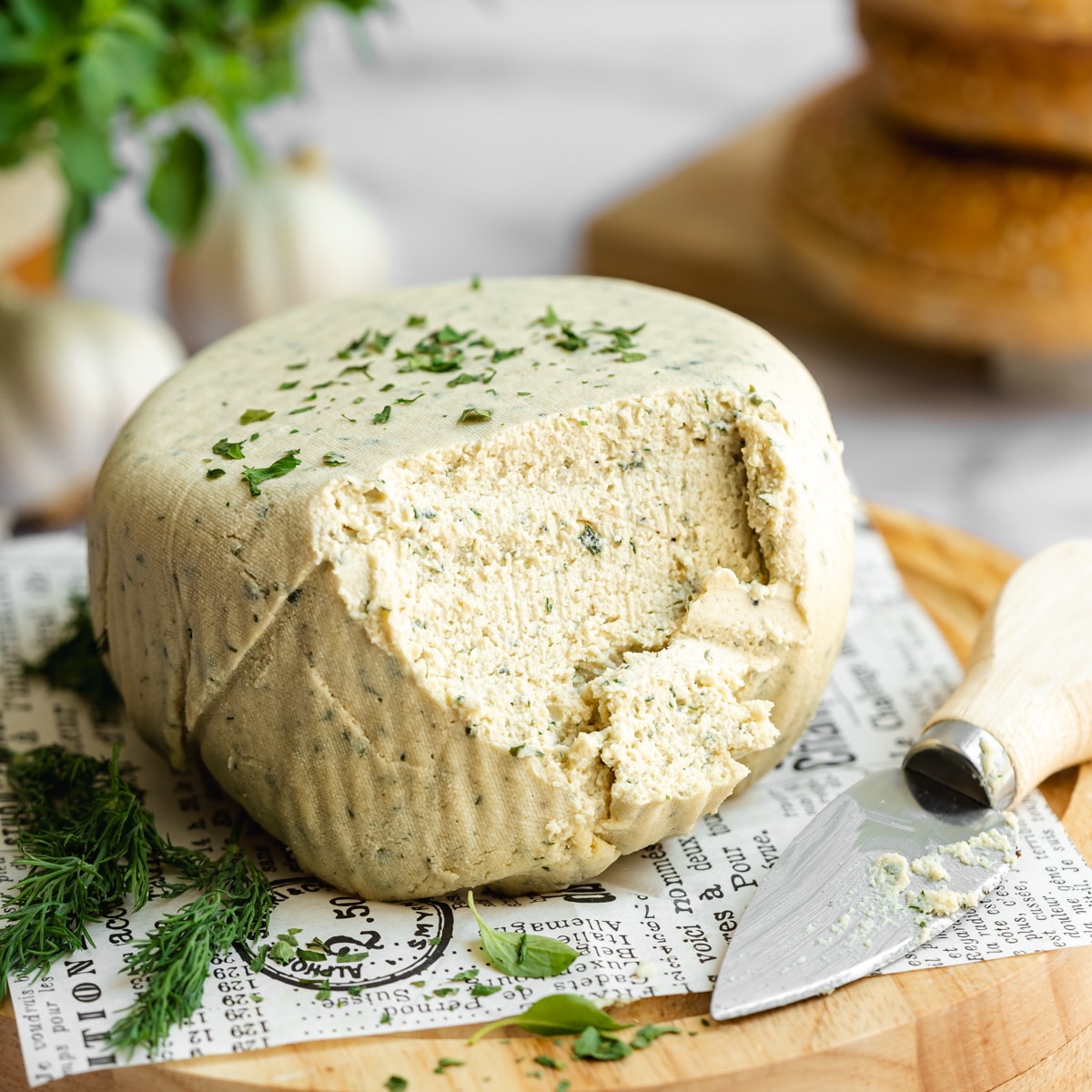 a block of homemade vegan boursin cream cheese on newspaper with a knife spreading some to show the creamy consistency.