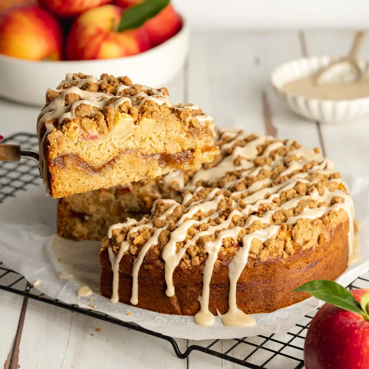 apple coffee cake with icing drizzled on top and a slice being lifted away with a cake slice.