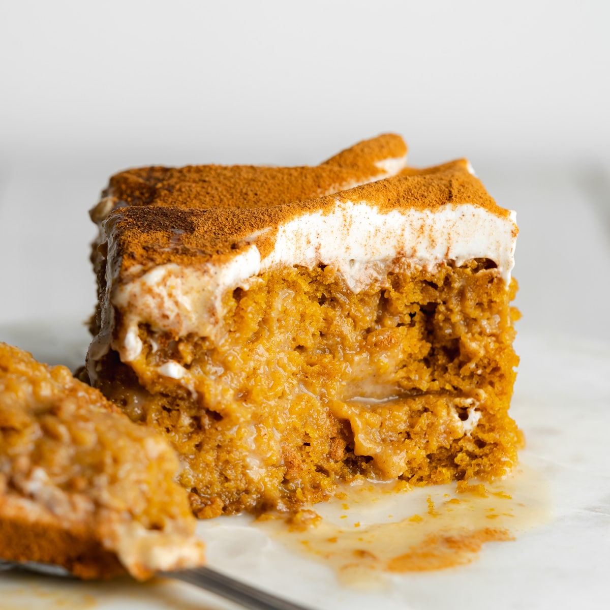 a slice of pumpkin spice tres leches cake on a marble place with a spoonful taken from it showing the moist interior.