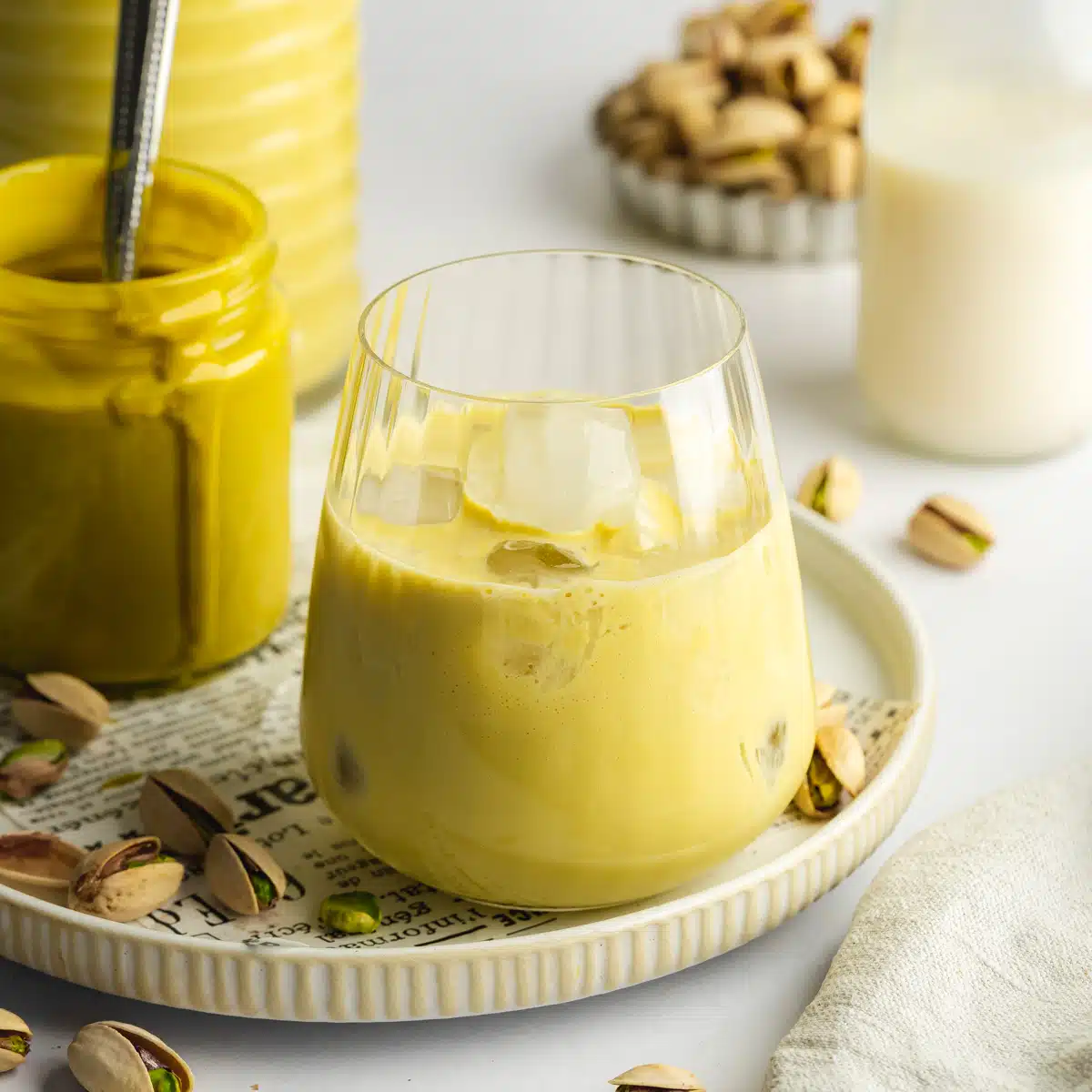 a glass of homemade pistachio liqueur on a plate with a jar of pistachio butter next to it.